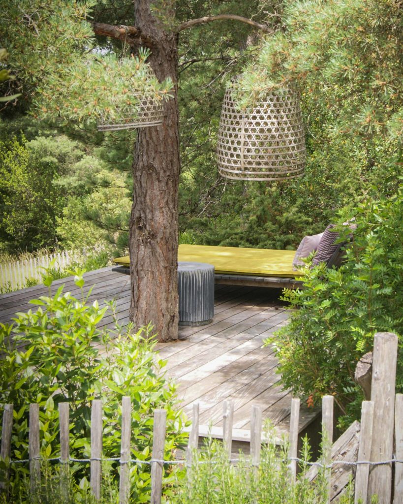 Terrasse en bois aménagée avec lit de repos sous les arbres dans un jardin paysager à Sarlat.